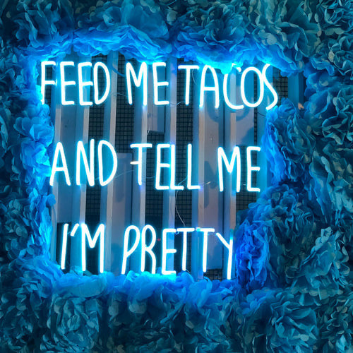 Blue custom neon sign reading “Feed Me Tacos and Tell Me I’m Pretty” displayed inside a Melbourne restaurant.
