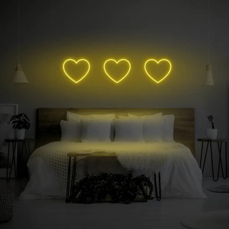 3 Hearts LED Neon Light Sign in yellow, featuring three heart outlines illuminated above a bed.