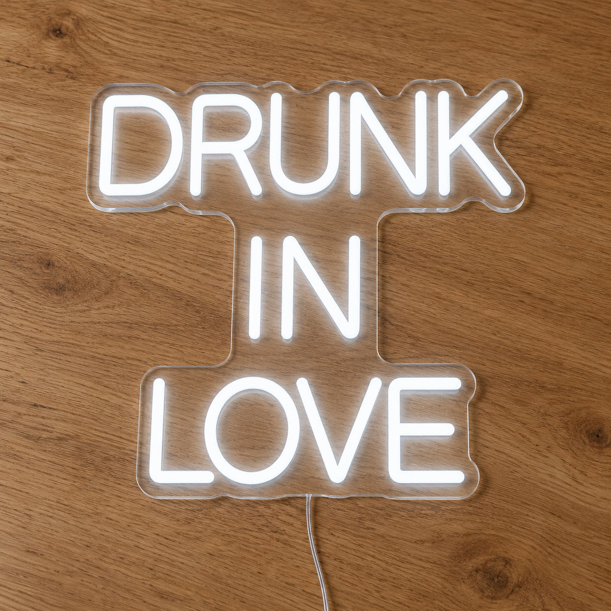 Drunk in Love LED Neon Light Sign in white, featuring three lines of block lettering on a wooden surface.