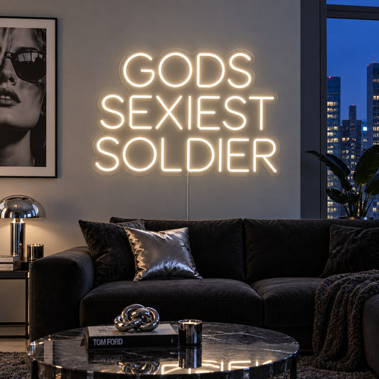 Warm White version of the Gods Sexiest Soldier Neon Sign, shown in rounded lettering above a dark sofa.