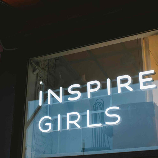 White LED neon sign reading 'Inspire' in flowing script, mounted on a soft pink studio wall at Inspire Girls Sydney