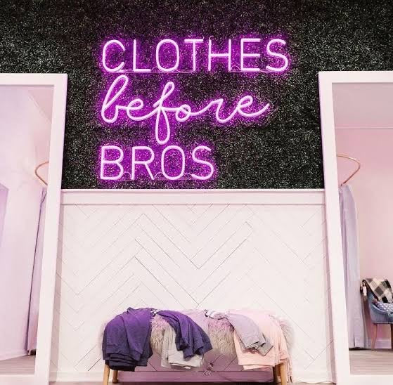 Neon sign with 'Clothes before Bros' text in a room setting in Sydney