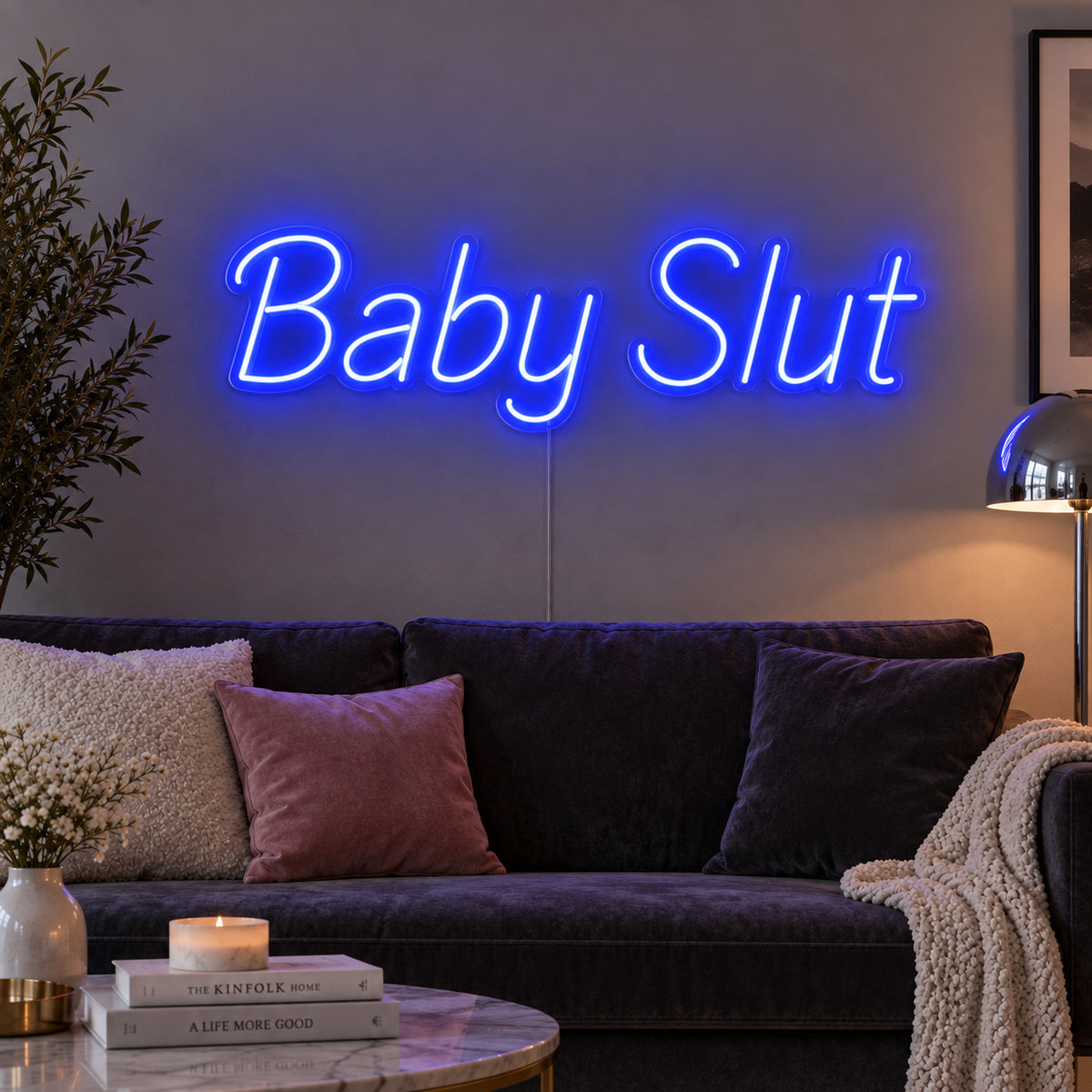 Baby Slut Neon Sign glowing blue above a grey sofa with pink cushions.