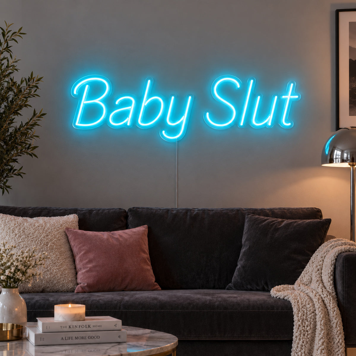Ice Blue version of the Baby Slut Neon Sign, shown above a grey sofa with pink cushions.