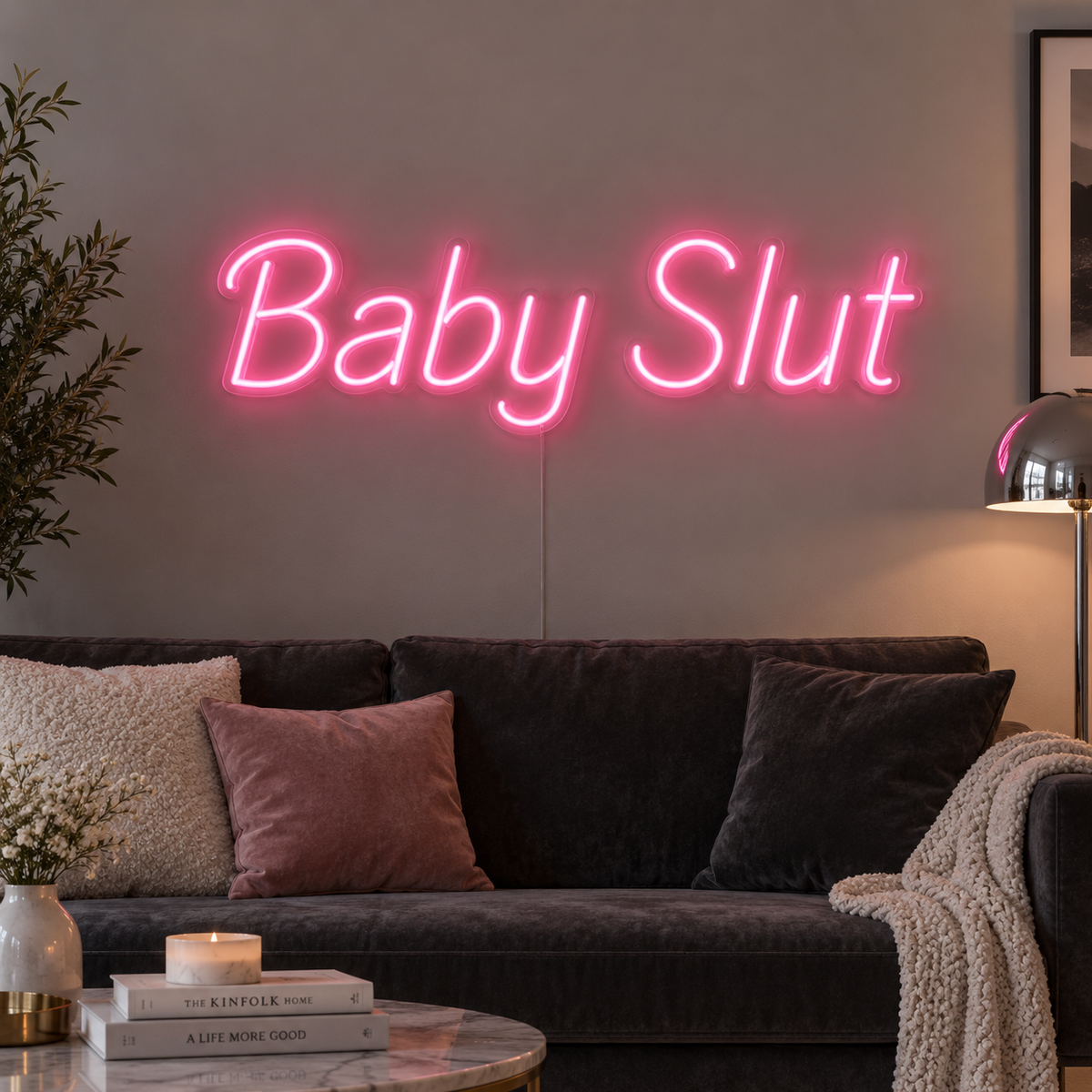 Baby Slut Neon Sign in pink above a grey sofa with pink cushions.