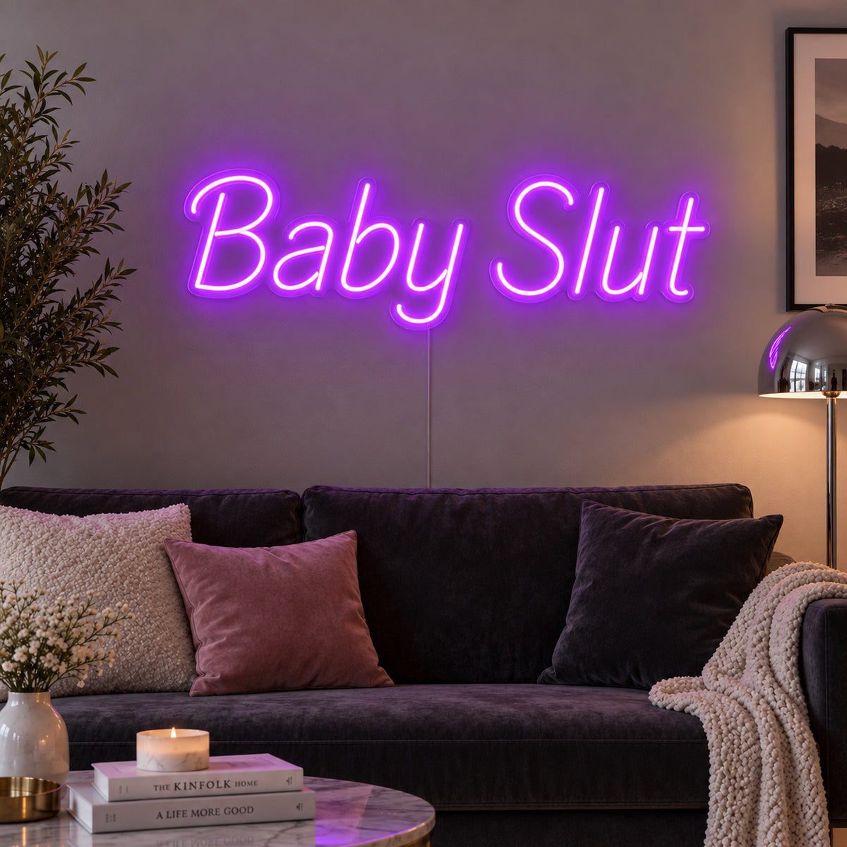 Baby Slut Neon Sign with purple lighting, displayed above a grey sofa with pink cushions.