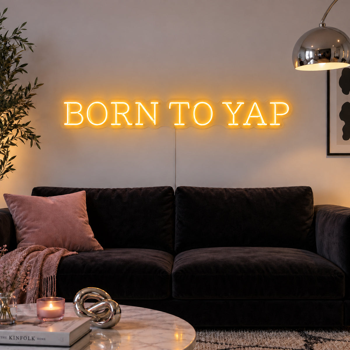 Born To Yap Neon Sign glowing gold above a dark sofa and glass coffee table.