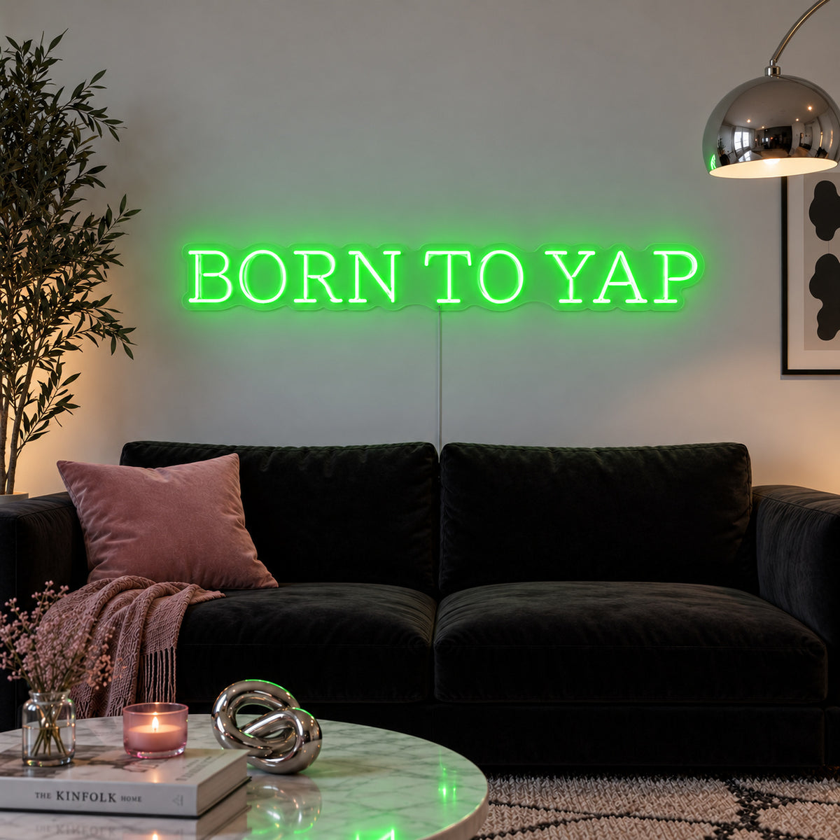 Born To Yap Neon Sign with green lighting, displayed above a dark sofa and glass coffee table.