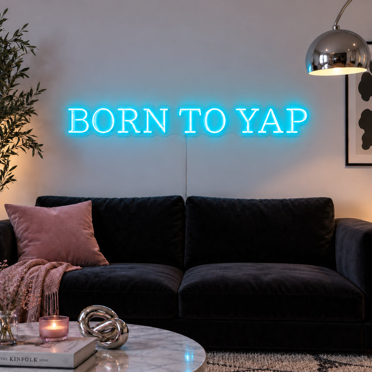 Ice Blue version of the Born To Yap Neon Sign, shown above a dark sofa and glass coffee table.