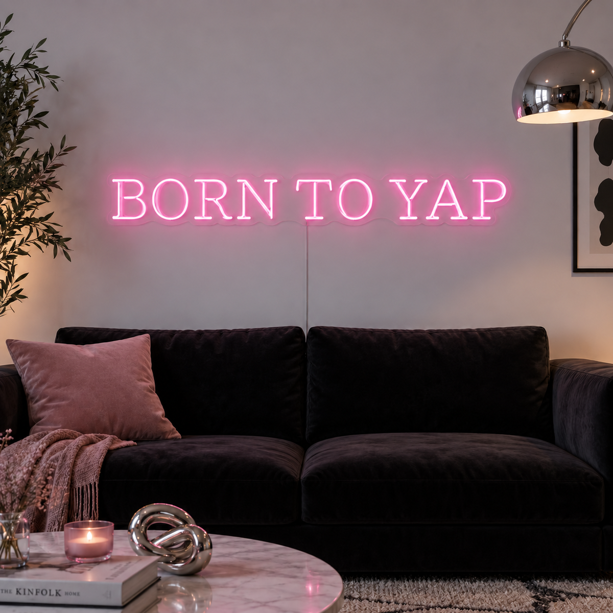 Born To Yap Neon Sign in pink above a dark sofa and glass coffee table.