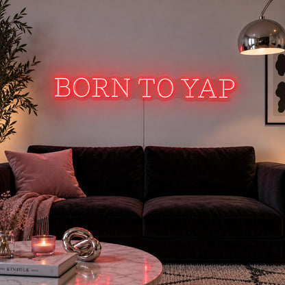 Born To Yap Neon Sign with red lighting, displayed above a dark sofa and glass coffee table.