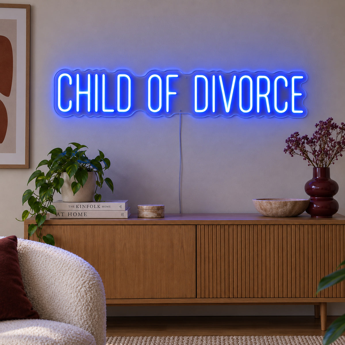 Child Of Divorce Neon Sign glowing blue above a wooden sideboard with plants.