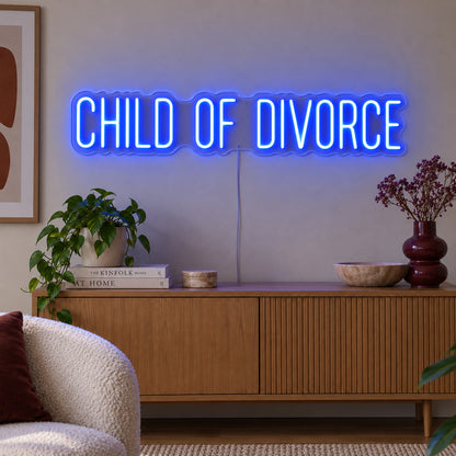 Child Of Divorce Neon Sign glowing blue above a wooden sideboard with plants.