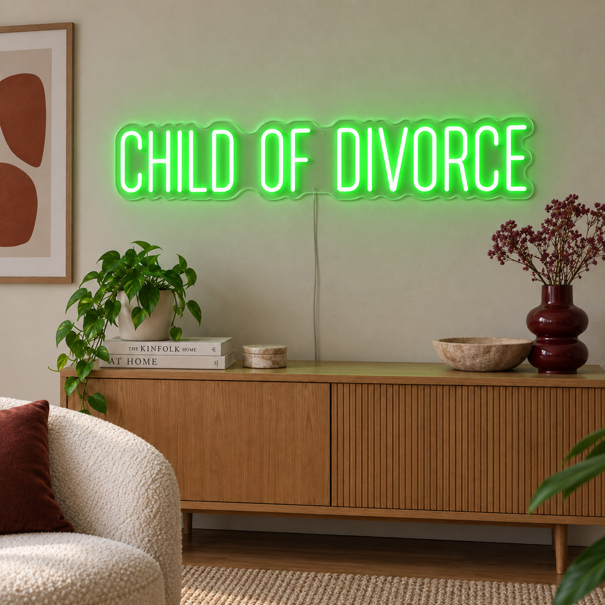 Child Of Divorce Neon Sign with green lighting, displayed above a wooden sideboard with plants.