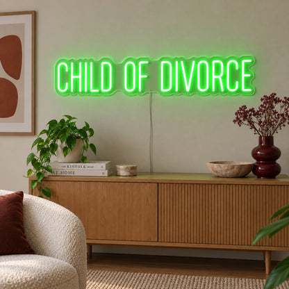 Child Of Divorce Neon Sign with green lighting, displayed above a wooden sideboard with plants.