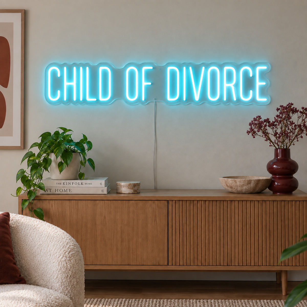 Ice Blue version of the Child Of Divorce Neon Sign, shown above a wooden sideboard with plants.