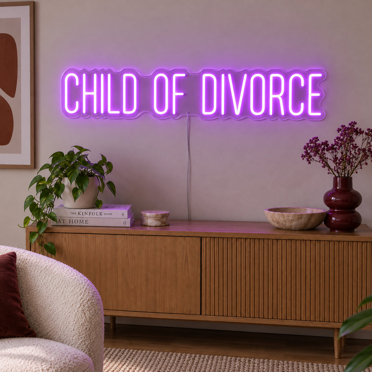 Child Of Divorce Neon Sign with purple lighting, displayed above a wooden sideboard with plants.