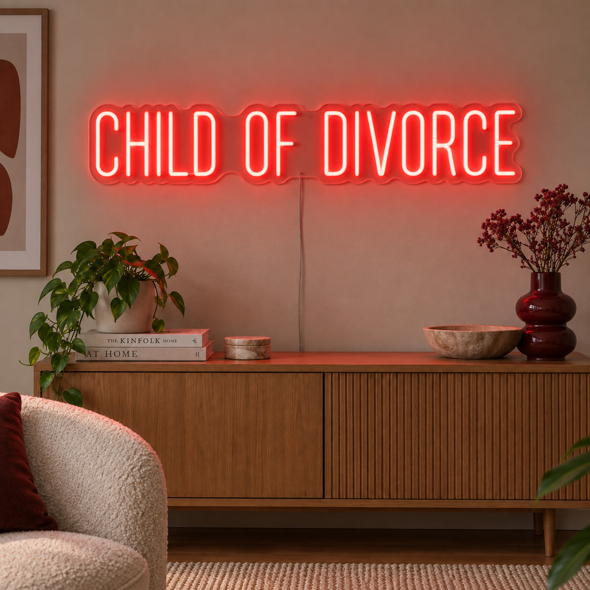 Child Of Divorce Neon Sign with red lighting, displayed above a wooden sideboard with plants.