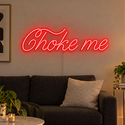 Choke Me Neon Sign in red, featuring Choke Me script lettering above a dark sofa.