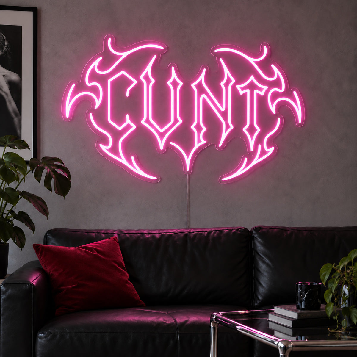 Cunt Neon Sign glowing pink in a tribal design above a black leather sofa.