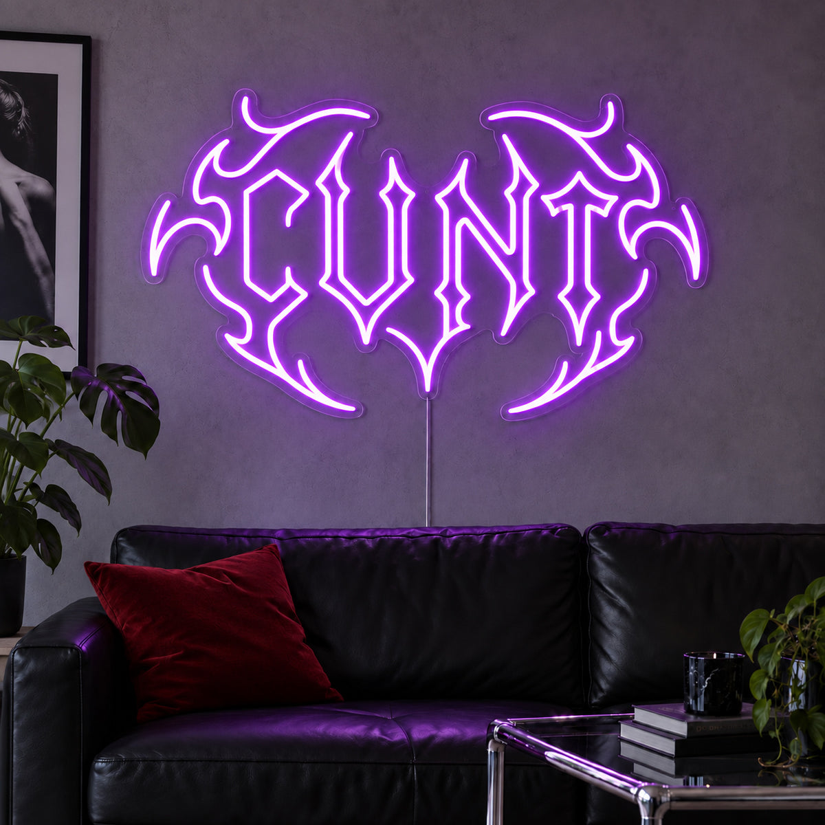 Cunt Neon Sign with purple lighting, displayed in a tribal design above a black leather sofa.