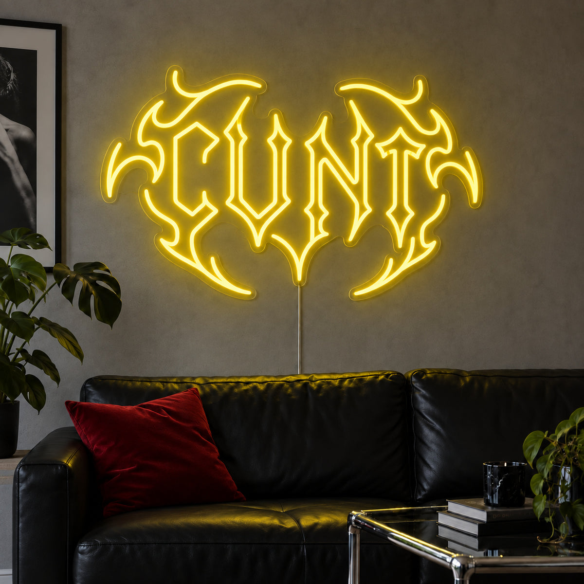 Cunt Neon Sign with yellow lighting, displayed in a tribal design above a black leather sofa.
