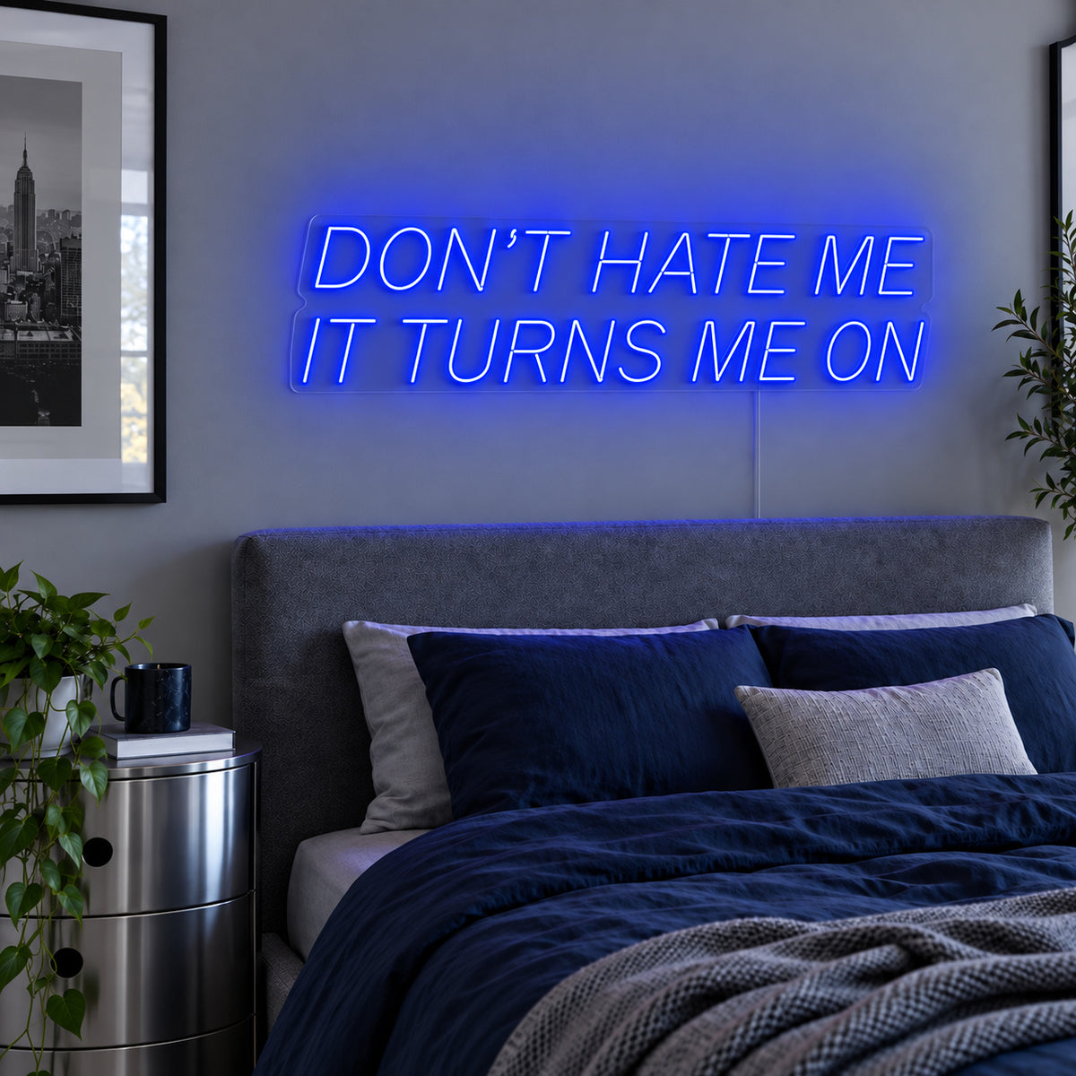 Don't Hate Me It Turns Me On Neon Sign glowing blue above a bed with dark blue bedding.