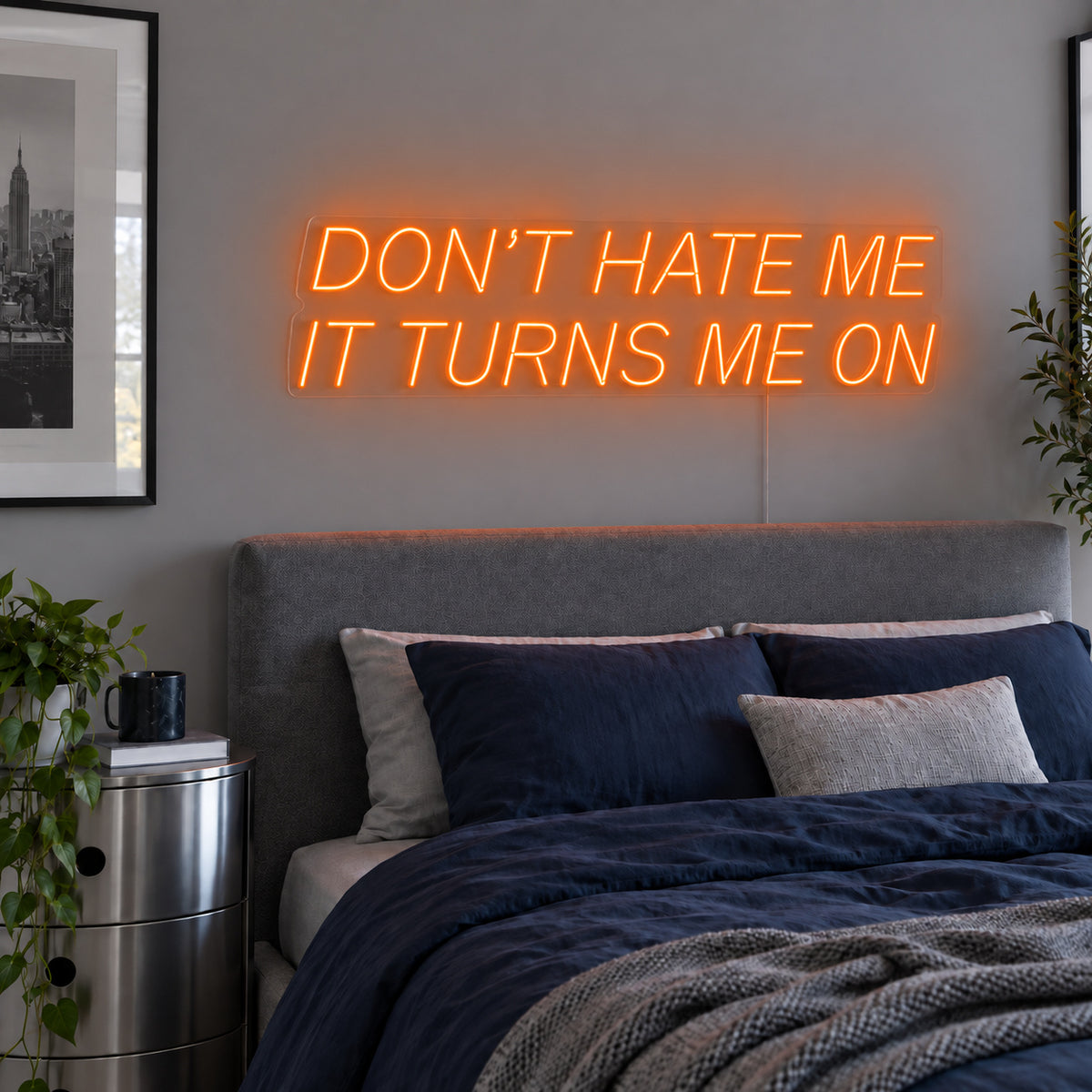 Orange version of the Don't Hate Me It Turns Me On Neon Sign, shown above a bed with dark blue bedding.