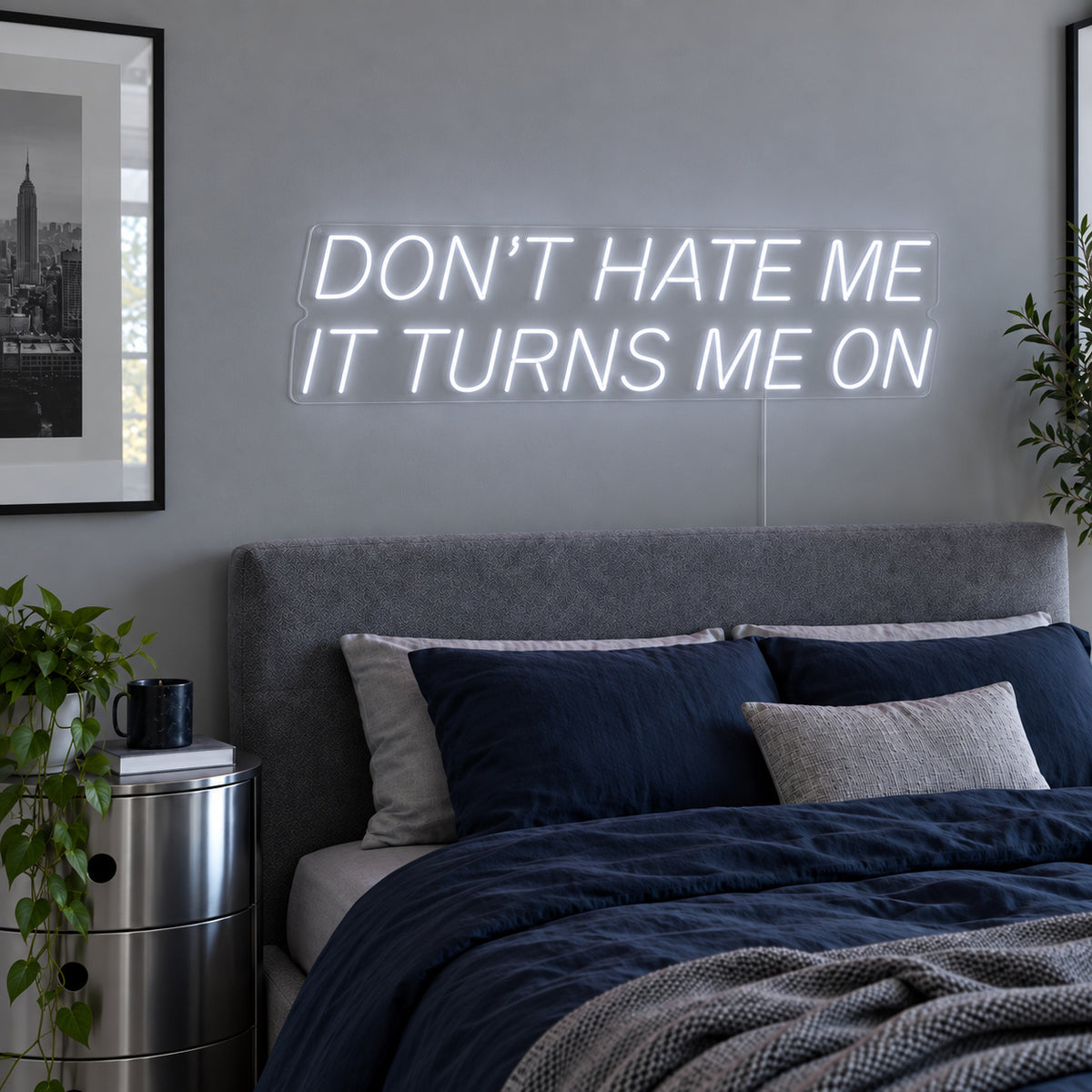 Don't Hate Me It Turns Me On Neon Sign glowing white above a bed with dark blue bedding.