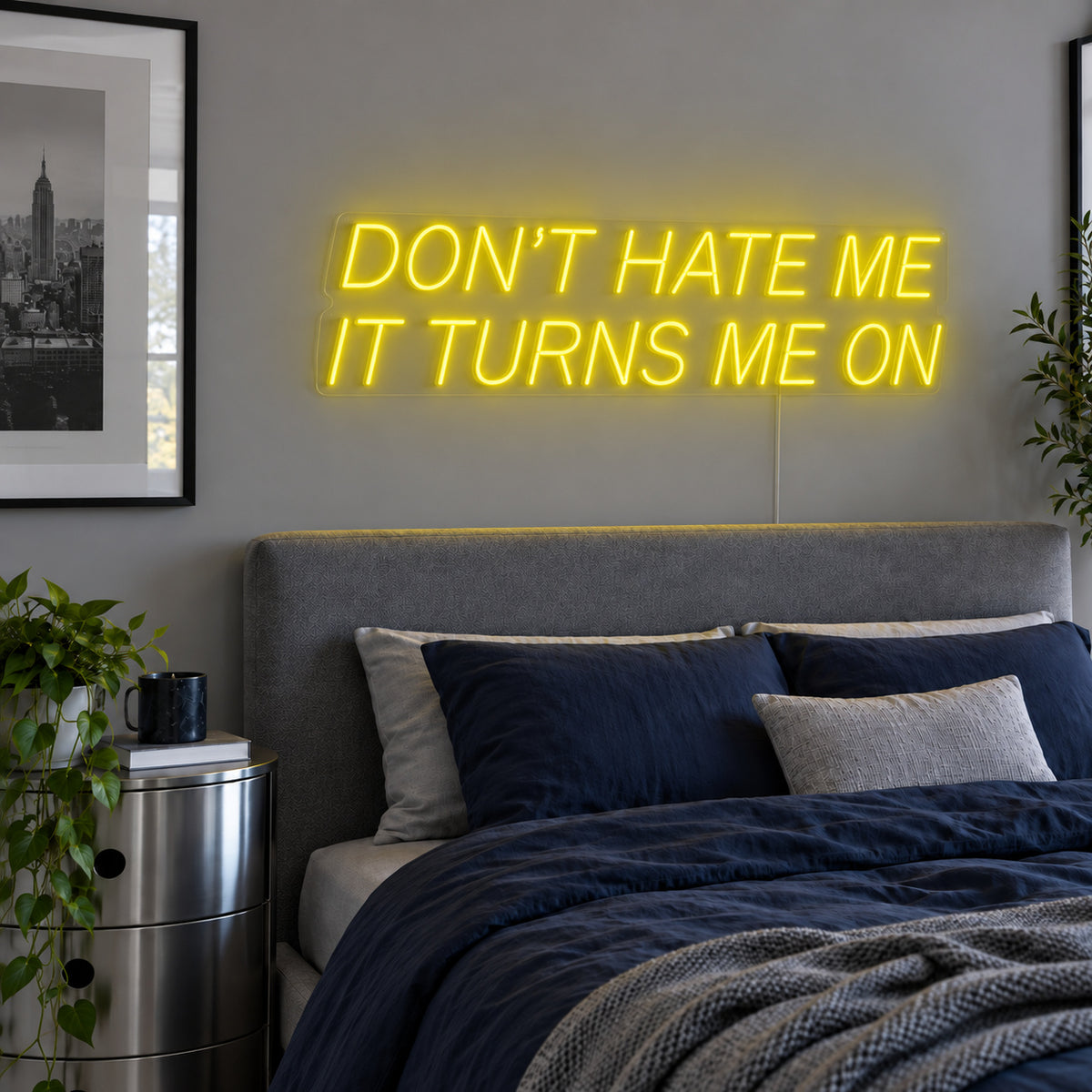 Don't Hate Me It Turns Me On Neon Sign with yellow lighting, displayed above a bed with dark blue bedding.