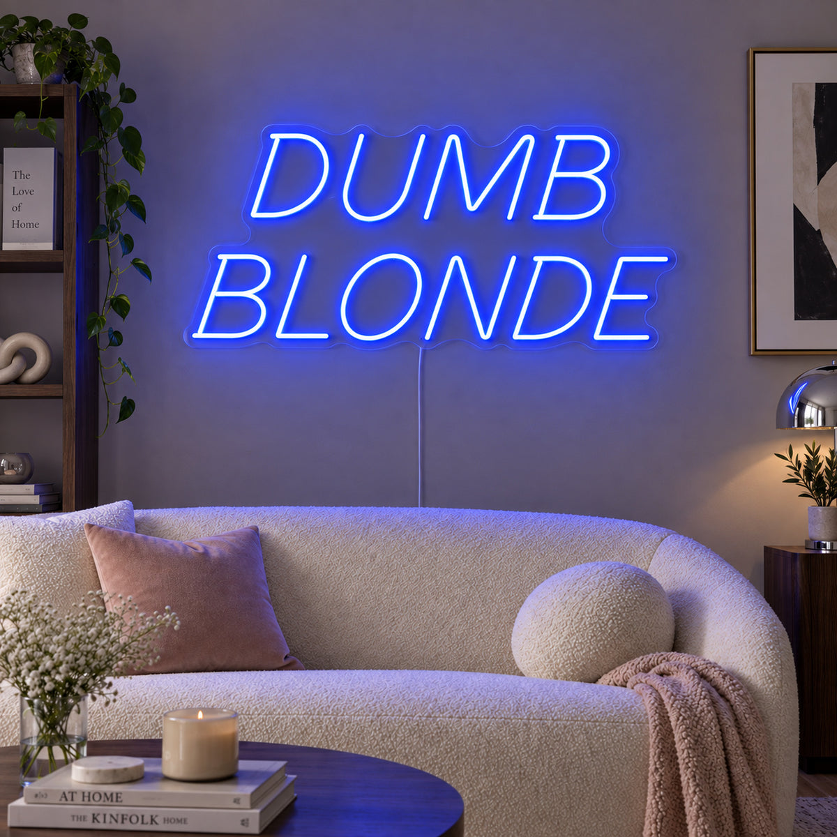 Dumb Blonde Neon Sign glowing blue in slanted lettering above a cream sofa.