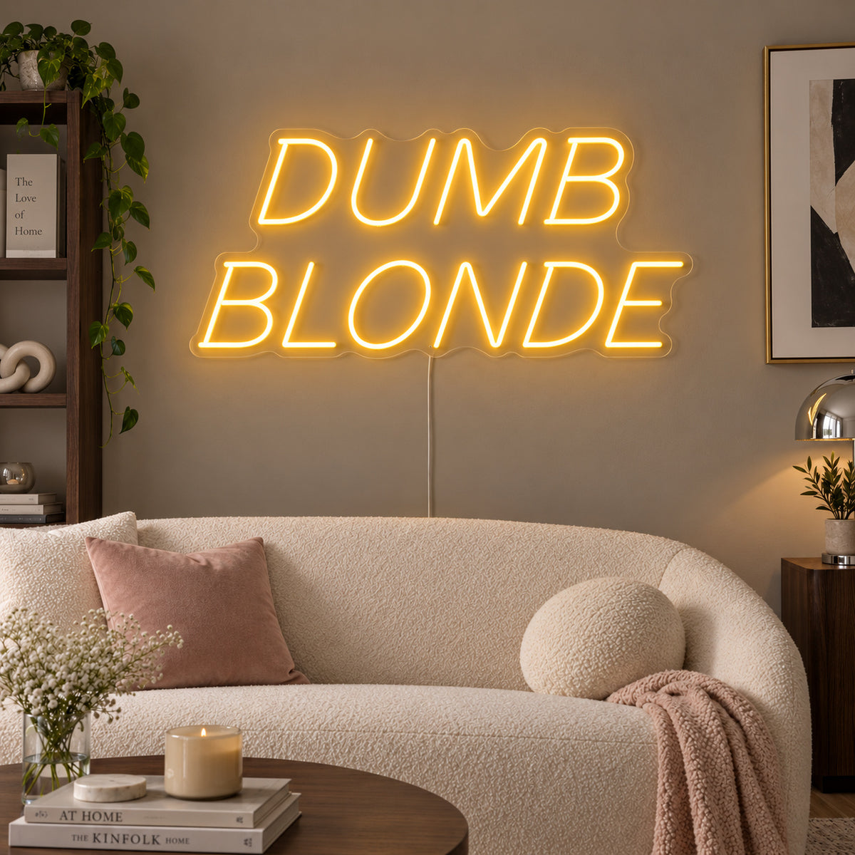 Dumb Blonde Neon Sign glowing gold in slanted lettering above a cream sofa.
