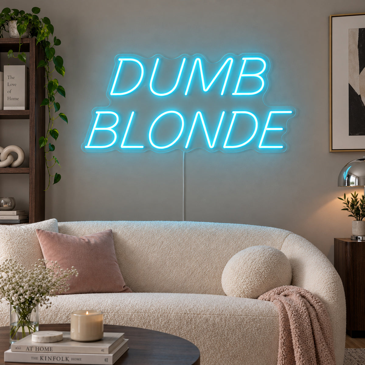 Ice Blue version of the Dumb Blonde Neon Sign, shown in slanted lettering above a cream sofa.