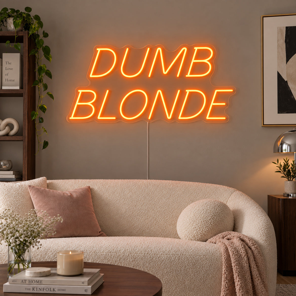 Orange version of the Dumb Blonde Neon Sign, shown in slanted lettering above a cream sofa.