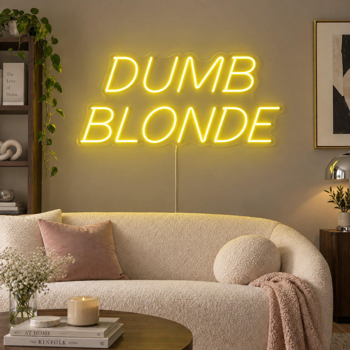 Dumb Blonde Neon Sign with yellow lighting, displayed in slanted lettering above a cream sofa.