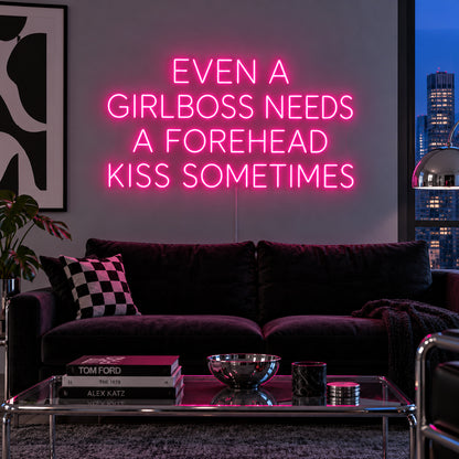 Even A Girlboss Needs A Forehead Kiss Sometimes Neon Sign glowing pink above a dark sofa and mirrored coffee table.