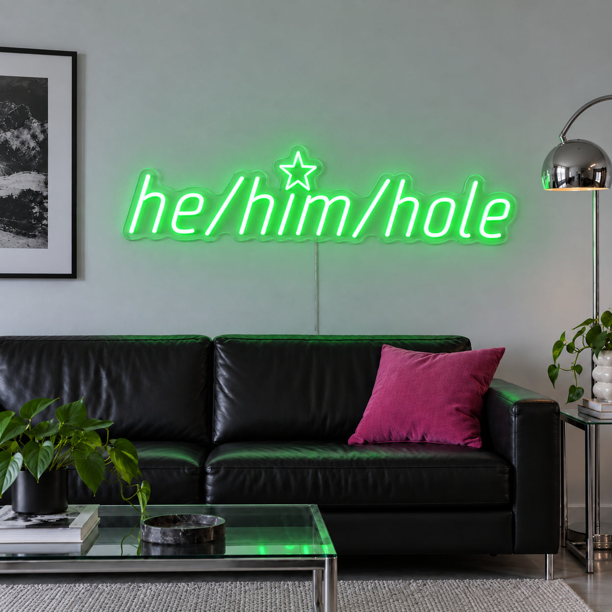He/Him/Hole Neon Sign with green lighting, displayed above a black leather sofa.