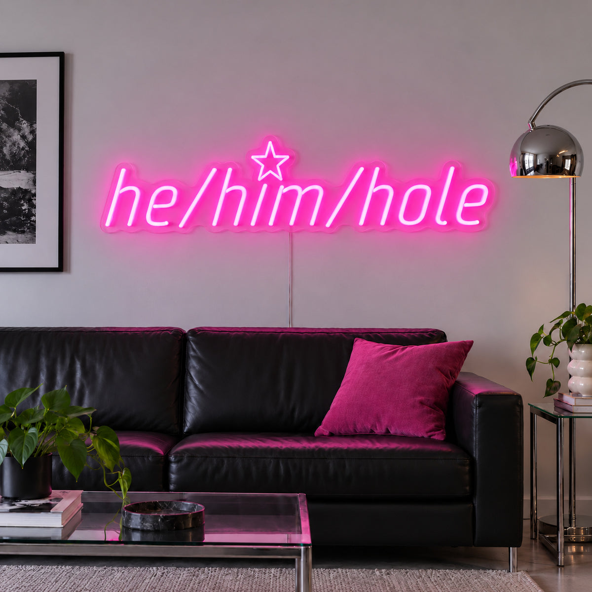 Rose Red version of the He/Him/Hole Neon Sign, shown above a black leather sofa.