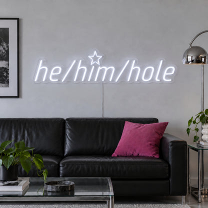 He/Him/Hole Neon Sign in white, featuring He/Him/Hole script lettering above a dark sofa.