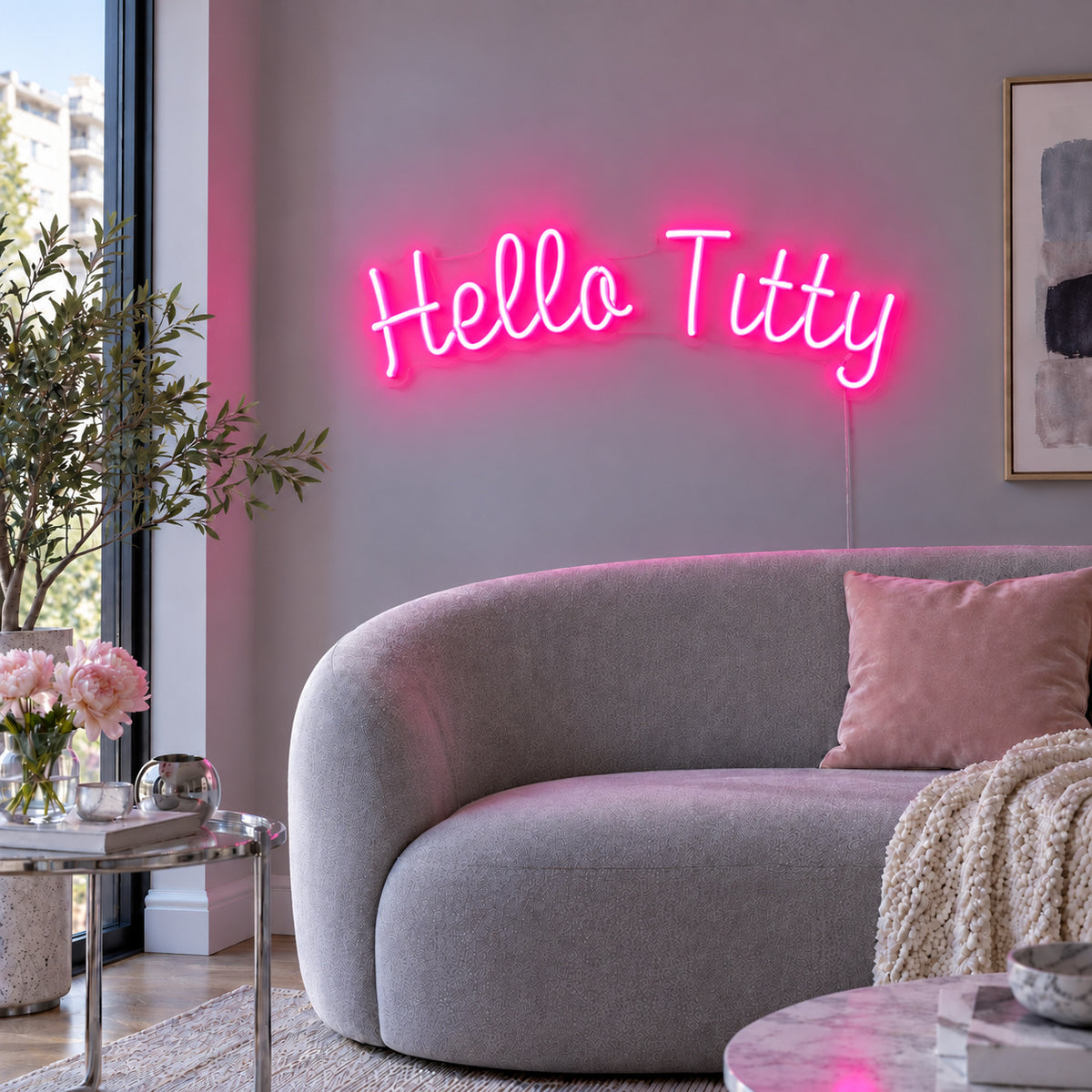 Rose Red version of the Hello Titty Neon Sign, shown above a curved grey sofa.
