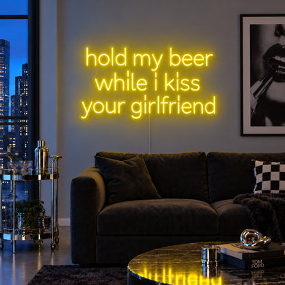 Hold My Beer While I Kiss Your Girlfriend Neon Sign with yellow lighting, displayed above a burgundy sofa.