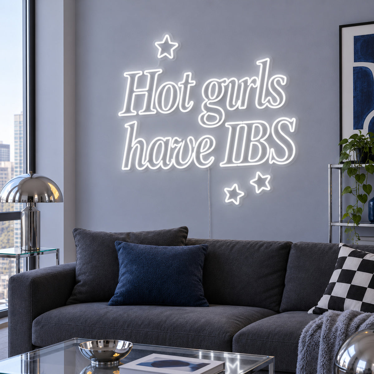 Hot Girls Have IBS Neon Sign glowing white with star details above a charcoal sofa.