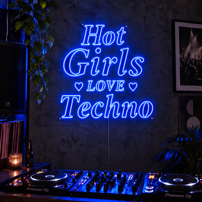Hot Girls Love Techno Neon Sign glowing blue with heart details above a DJ setup.