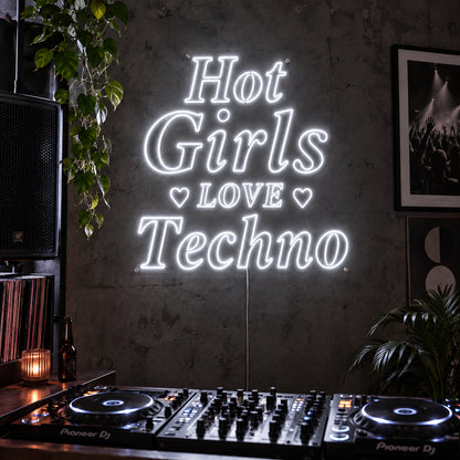 Hot Girls Love Techno Neon Sign glowing white with heart details above a DJ setup.