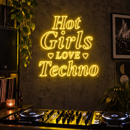 Hot Girls Love Techno Neon Sign with yellow lighting, displayed with heart details above a DJ setup.