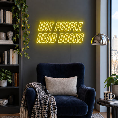 Hot People Read Books Neon Sign with yellow lighting, displayed above a blue reading chair.