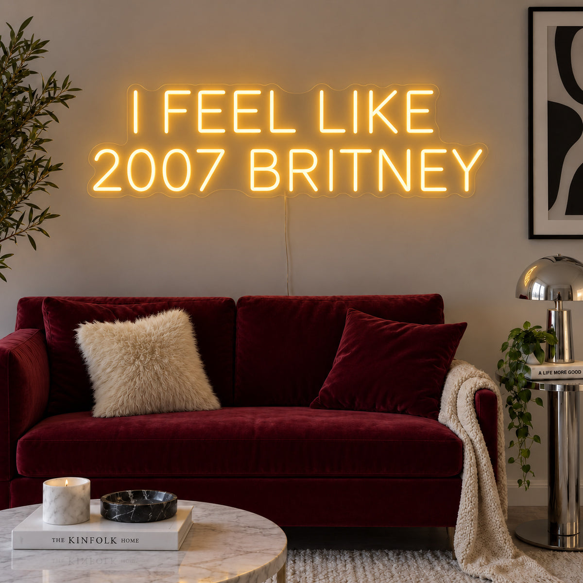 I Feel Like 2007 Britney Neon Sign glowing gold above a burgundy sofa.
