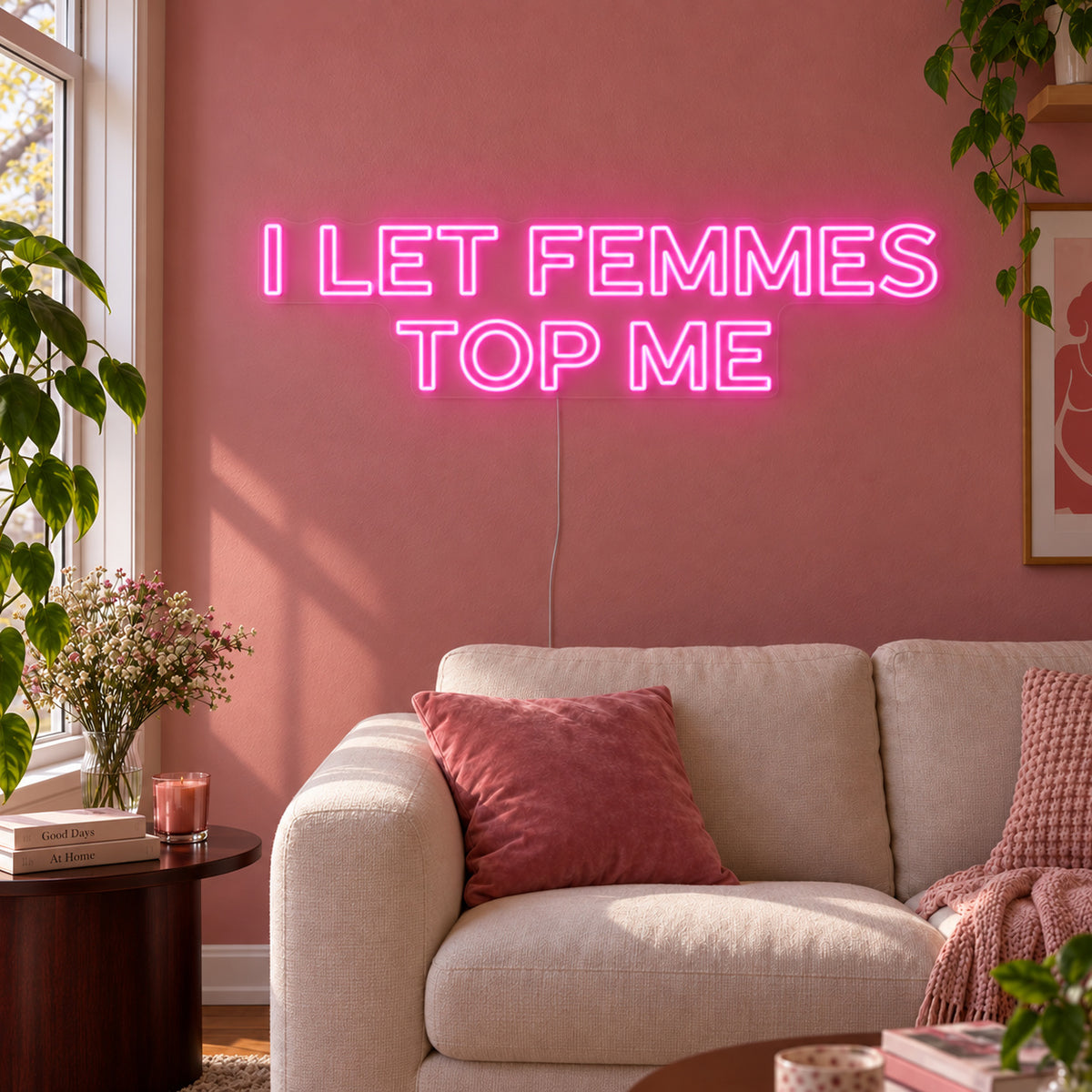 I Let Femmes Top Me Neon Sign glowing pink in outlined lettering above a cream chair.