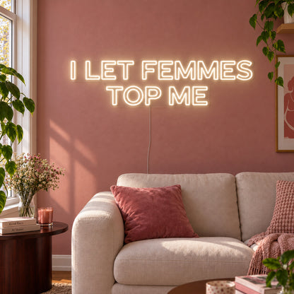 Warm White version of the I Let Femmes Top Me Neon Sign, shown in outlined lettering above a cream chair.