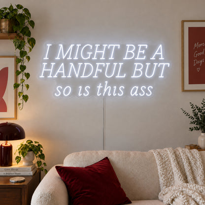 I Might Be A Handful But So Is This Ass Neon Sign, RGB colour-changing option shown in white in wide lettering above a cream sofa.